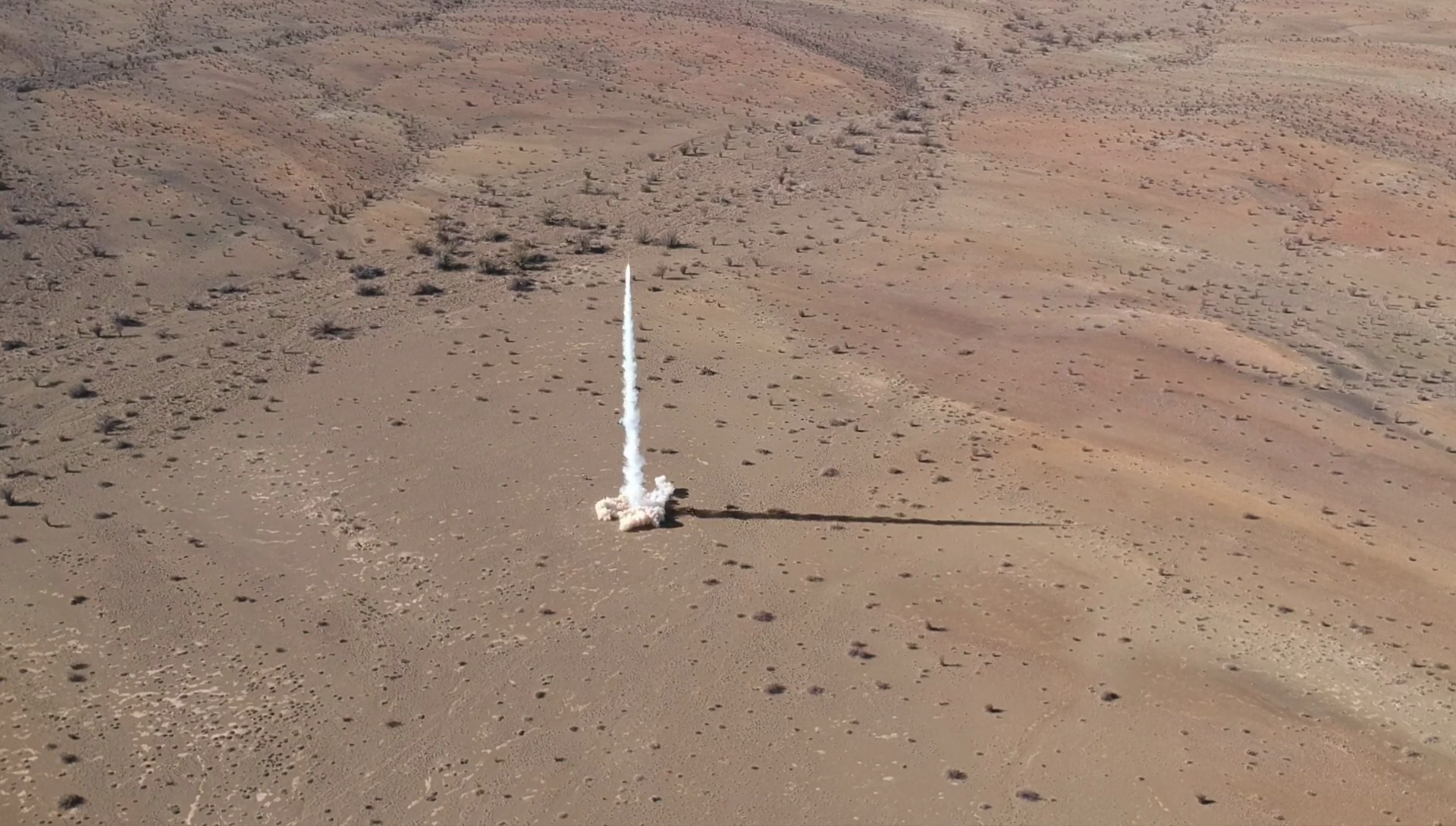 Rocket lifting off from the desert, seen from a chase drone