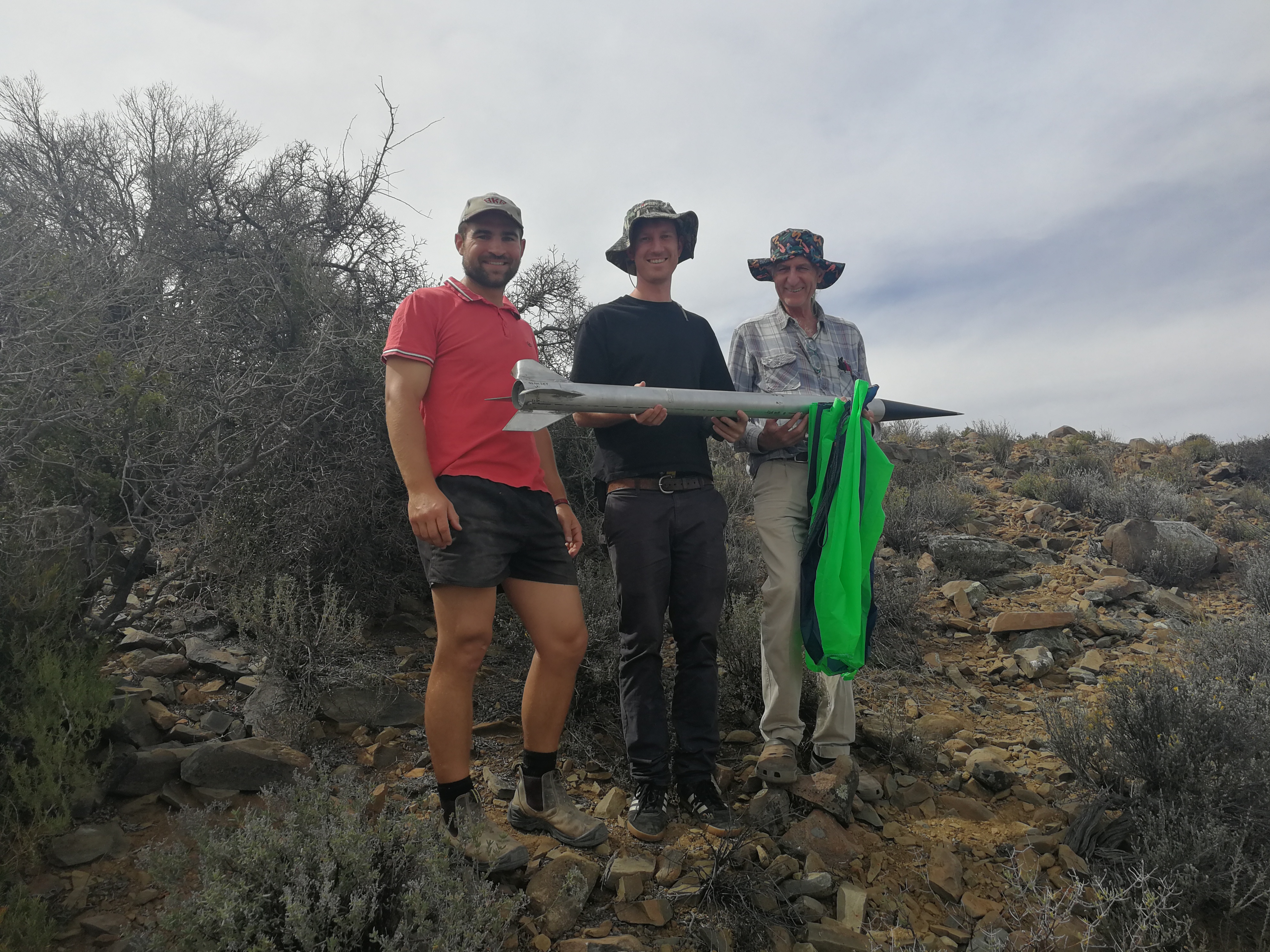 Three people holding a recovered rocket in the field